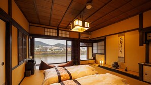 A traditional Japanese room with tatami flooring, a bed with floral bedding, a view of a river, and a shoji screen.