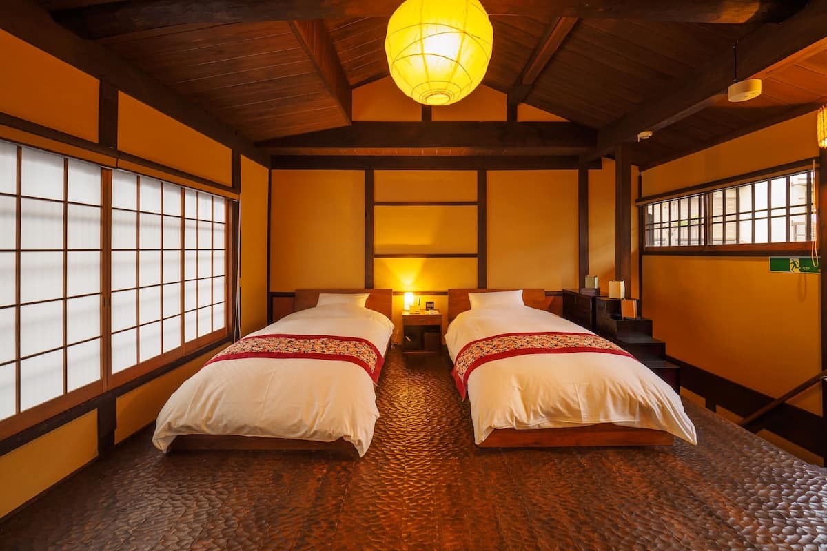 Una habitación tradicional japonesa con suelo de tatami, dos camas con ropa de cama blanca, un farol de papel colgante y puertas correderas shoji.