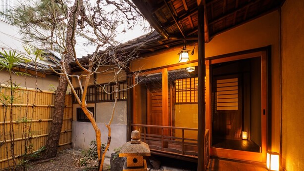 A traditional Japanese-style building with a wooden exterior, a stone lantern, and a bamboo fence.
