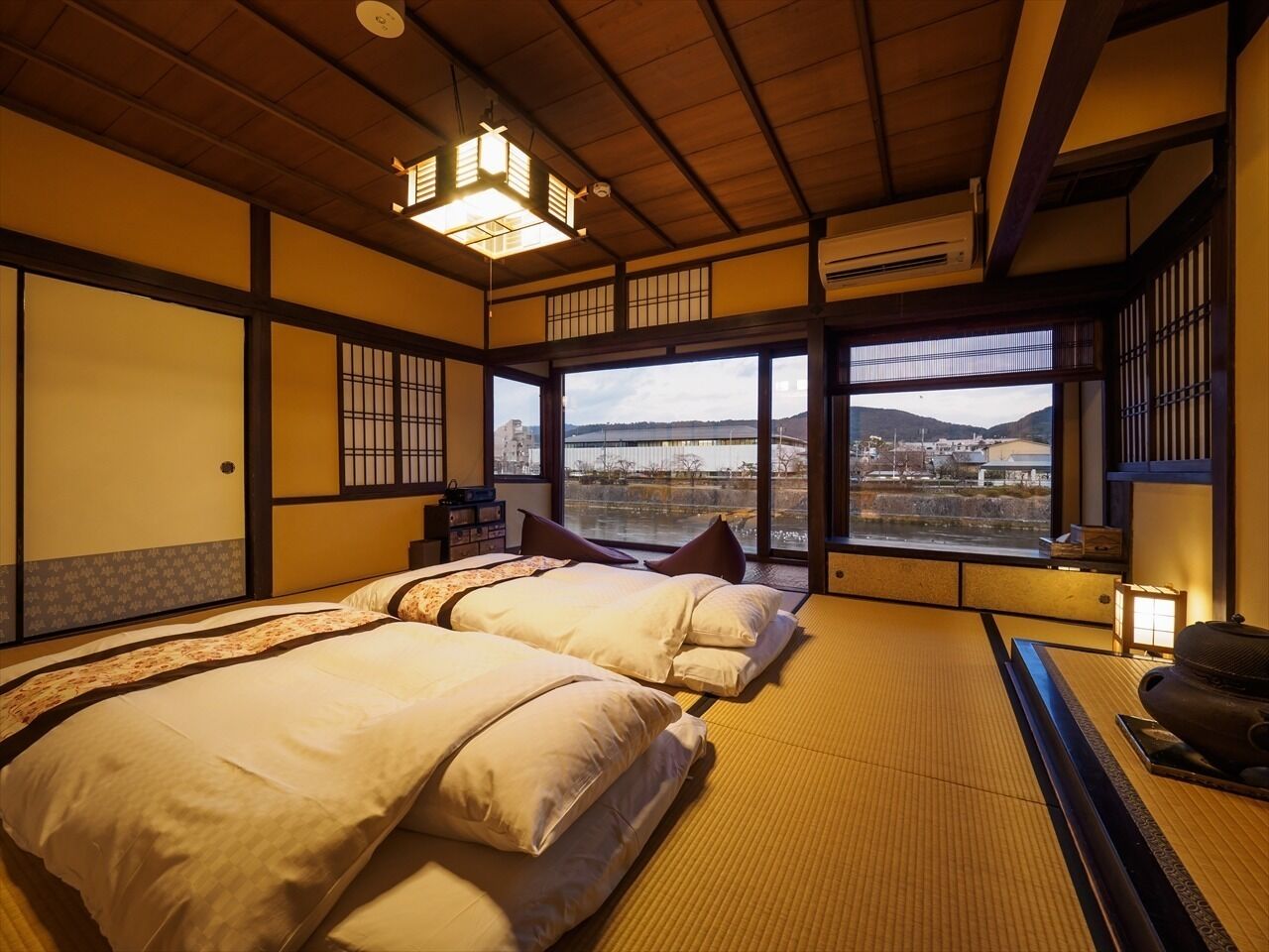 A traditional Japanese-style room with tatami flooring, a large window with a view, and a bed with pillows.