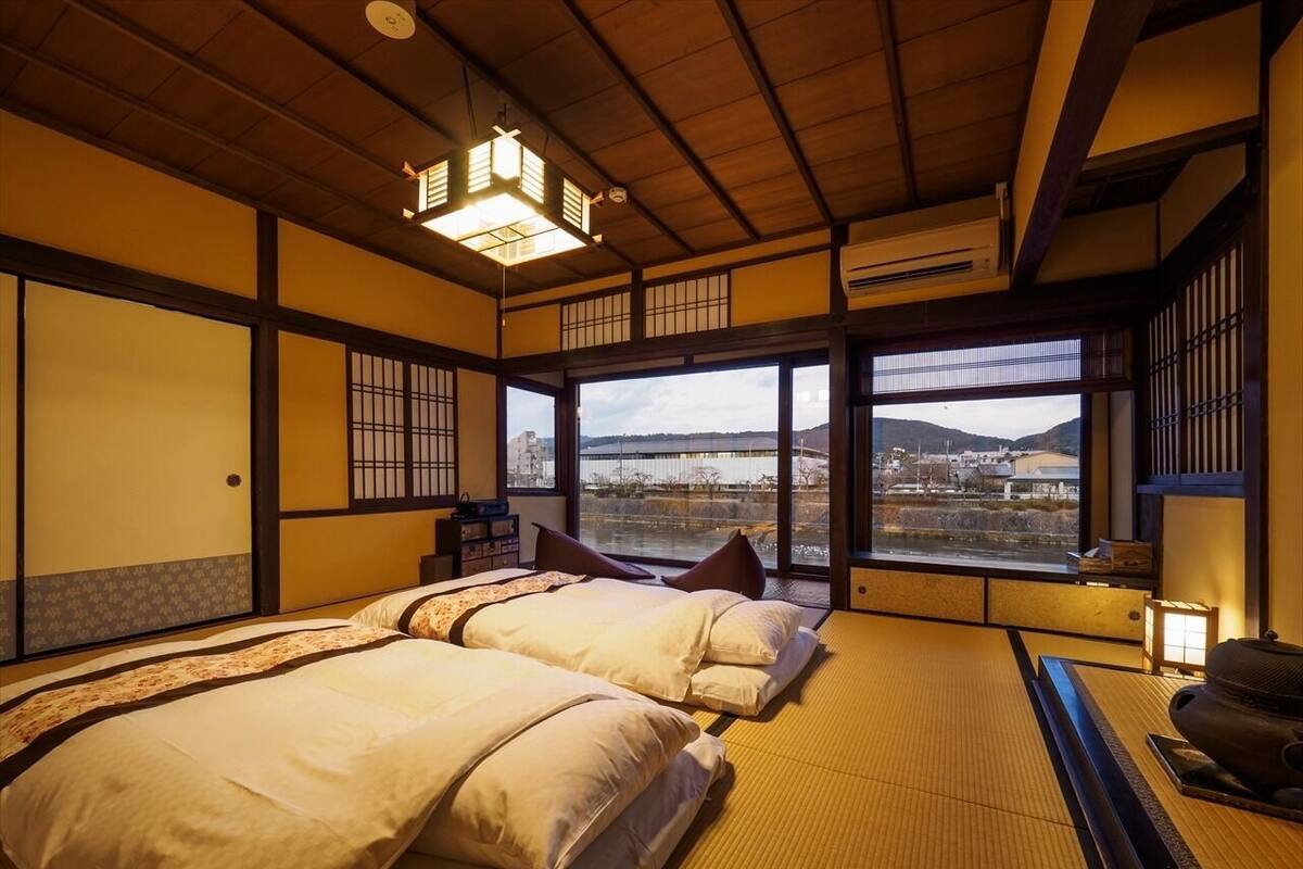 A traditional Japanese-style room with tatami flooring, a large window with a view, and a bed with pillows.