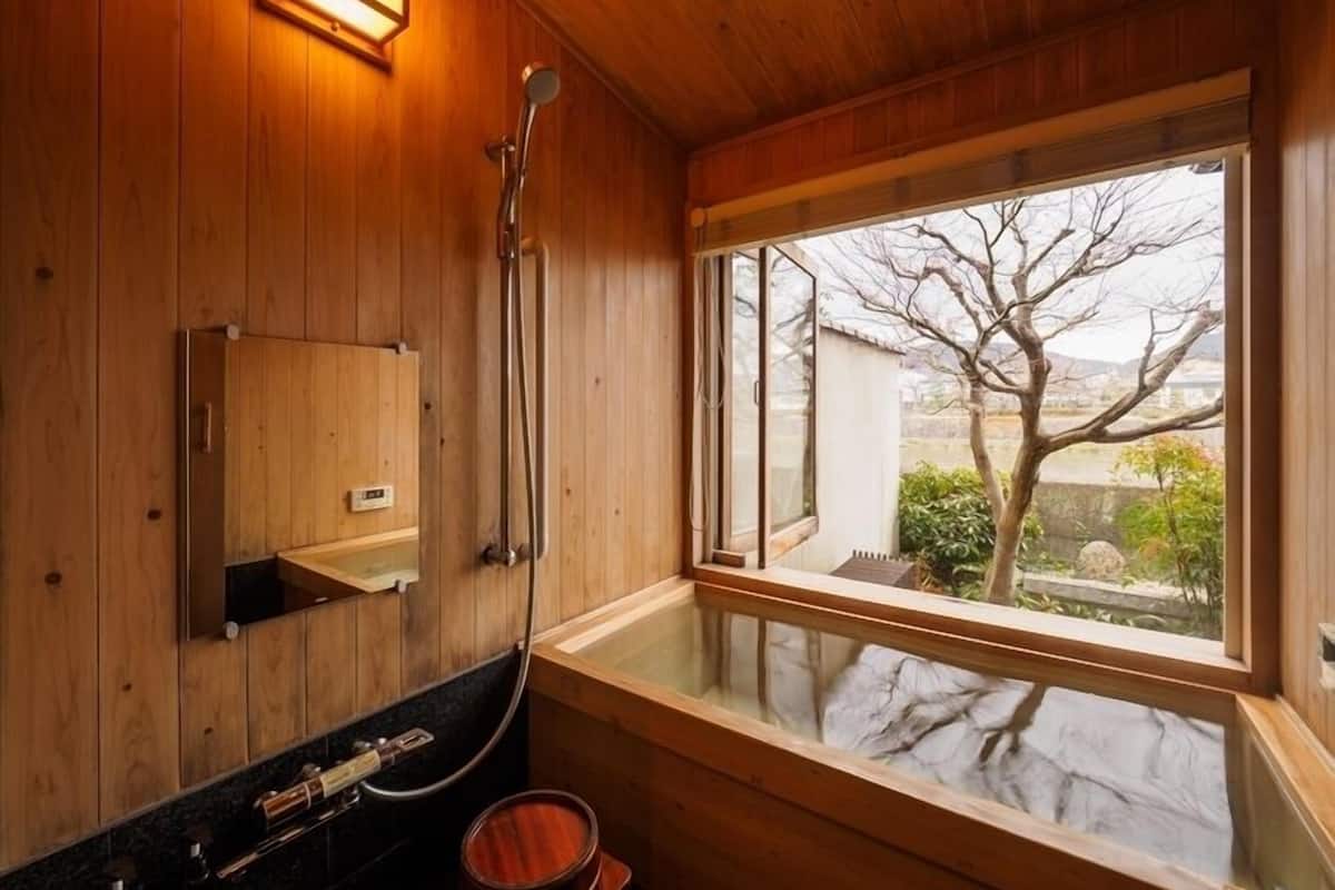 Interior de madera con un ventanal grande, una bañera de madera y una ducha.