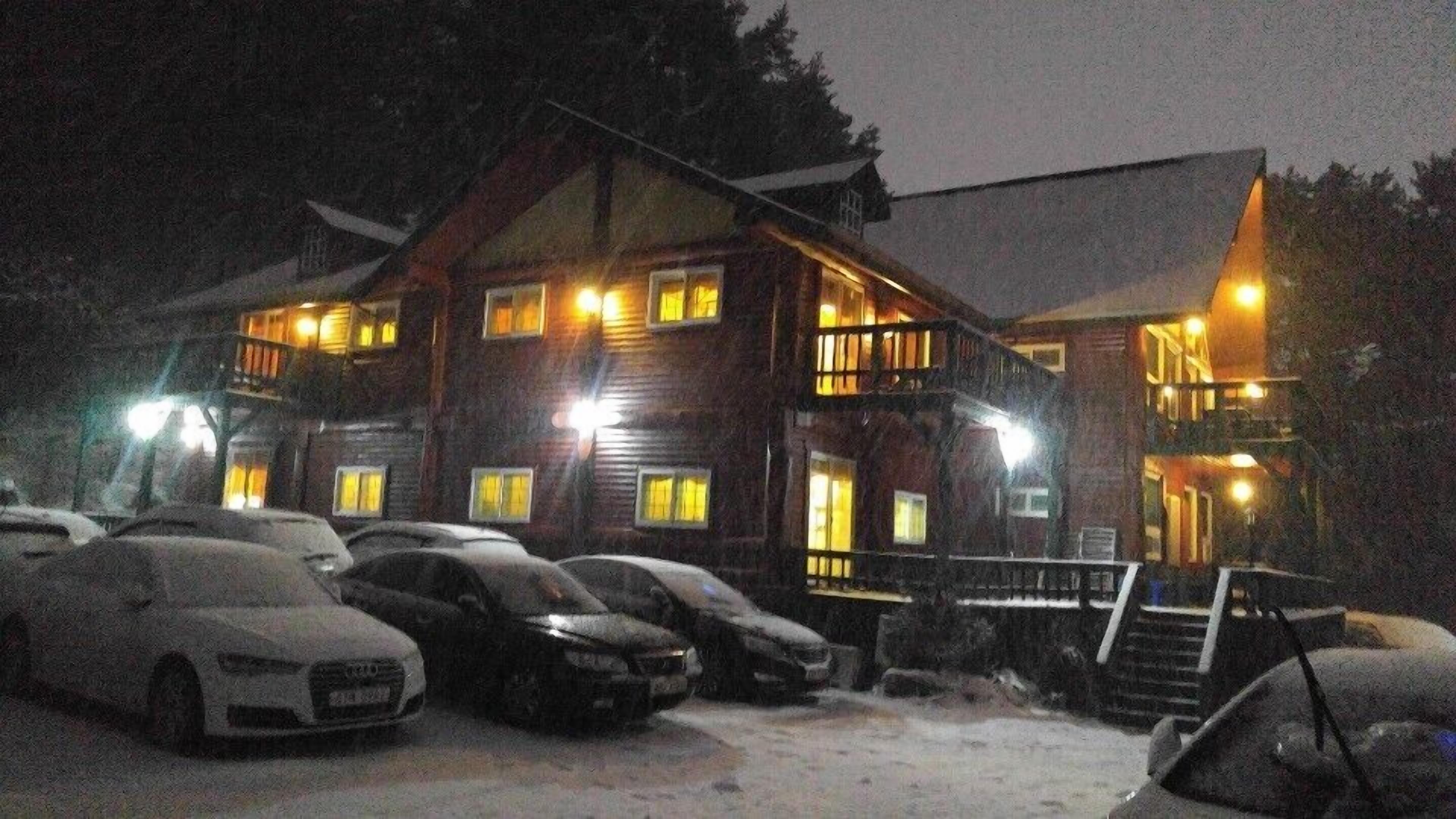 A two-story lodge with multiple windows and a balcony, surrounded by parked cars.