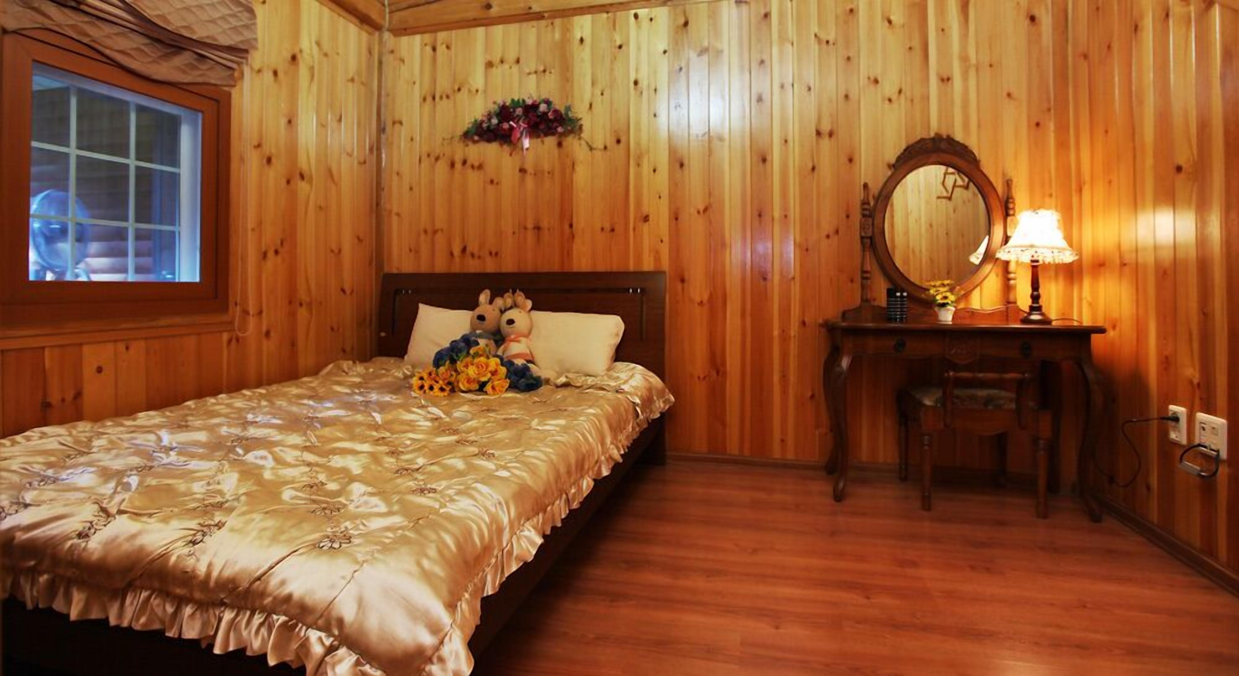 Una stanza con rivestimento in legno, un letto, una cassettiera, uno specchio e una finestra.