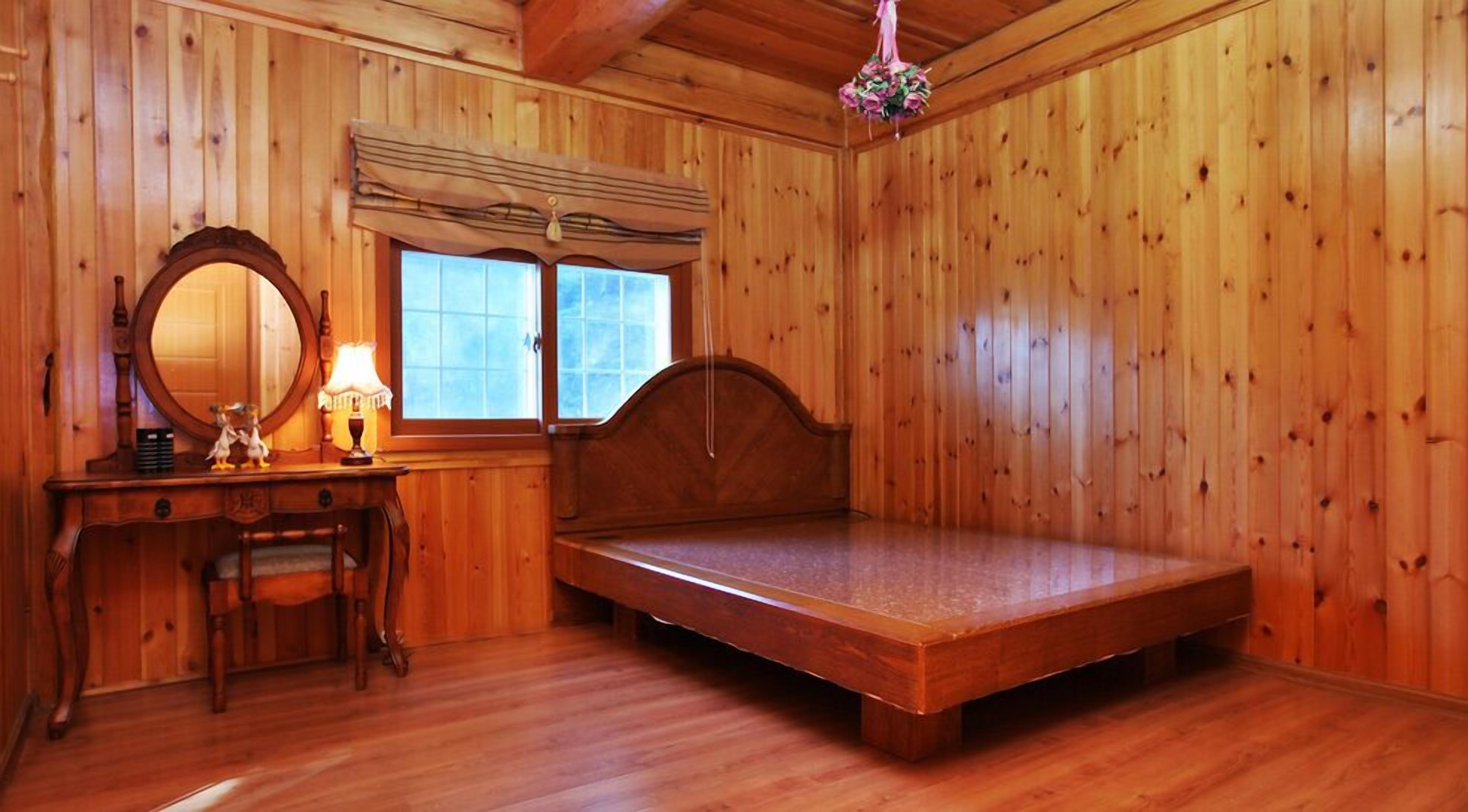 Una habitación de madera con una cama, un aparador, un espejo y una ventana.