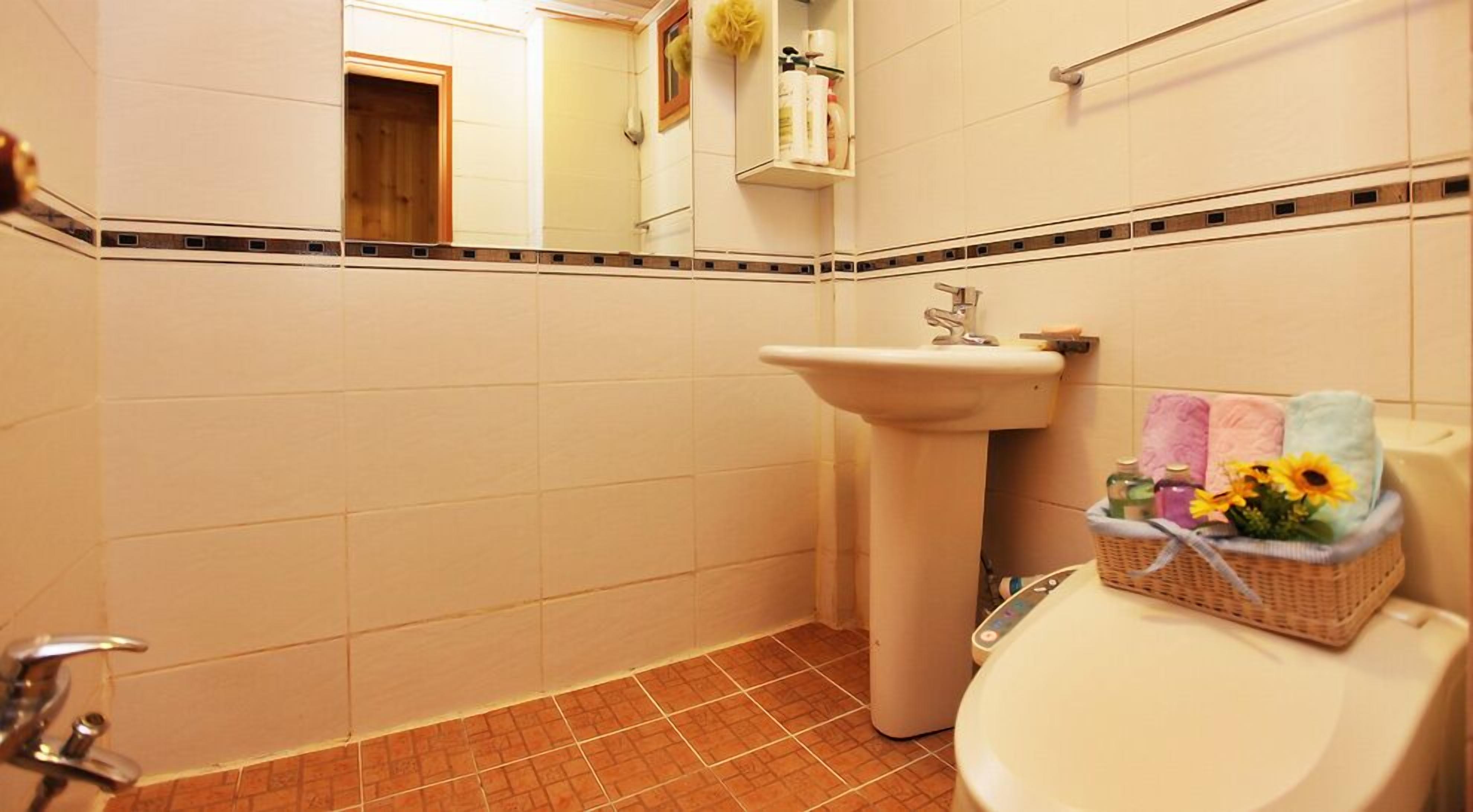 A bathroom with a white sink, a toilet, and a basket of toiletries on the toilet.