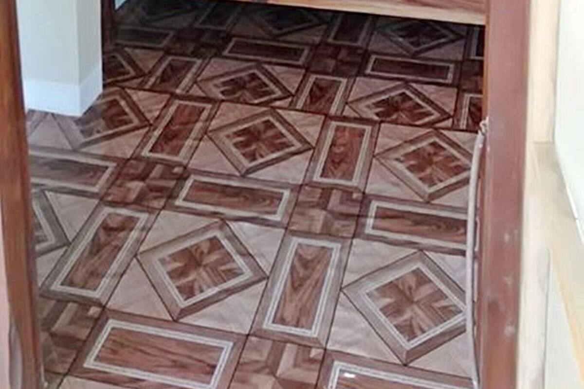 A small, single-bed room with a wooden headboard and a blue mattress. The floor has a geometric patterned tile design.