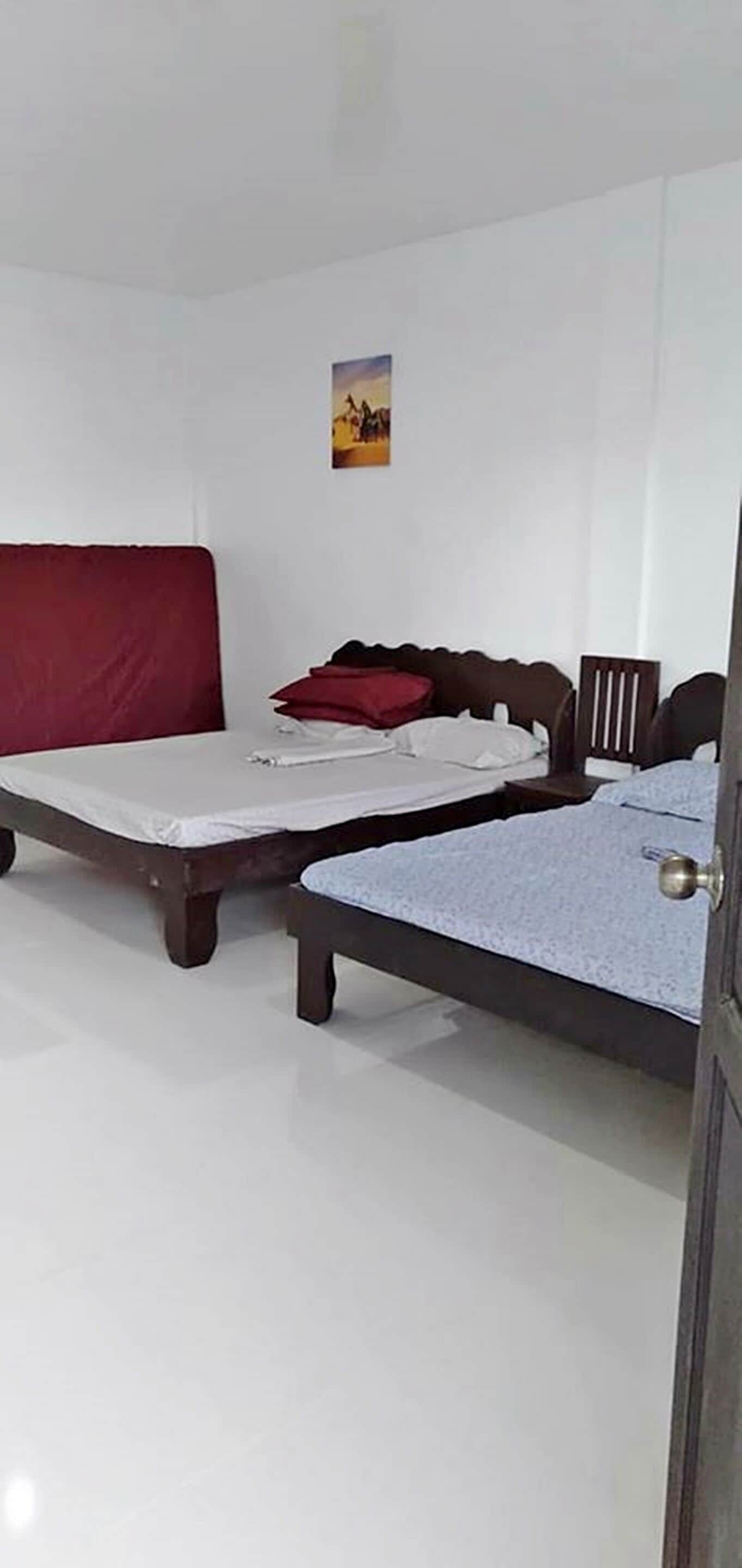 Un dormitorio con dos camas, un cabecero rojo y una mesita de noche pequeña.