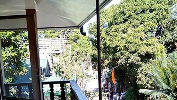 Un balcon fermé avec un sol à motifs, une balustrade et une vue sur un jardin et des arbres.
