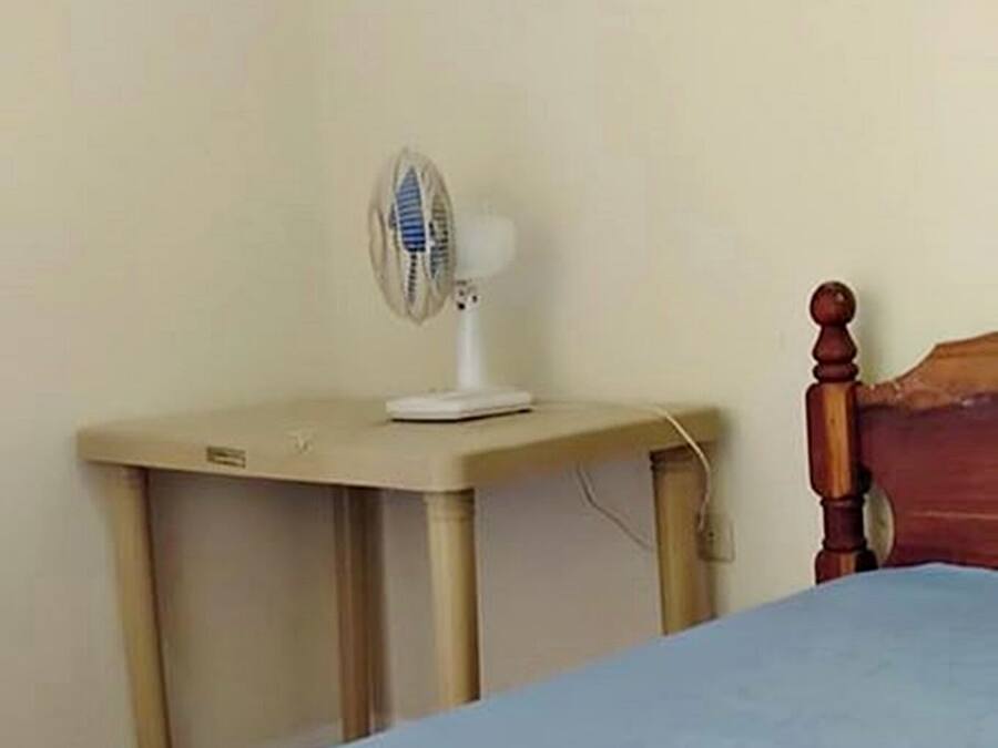 A bedroom with a bed, a bedside table with a fan, and a wooden headboard.
