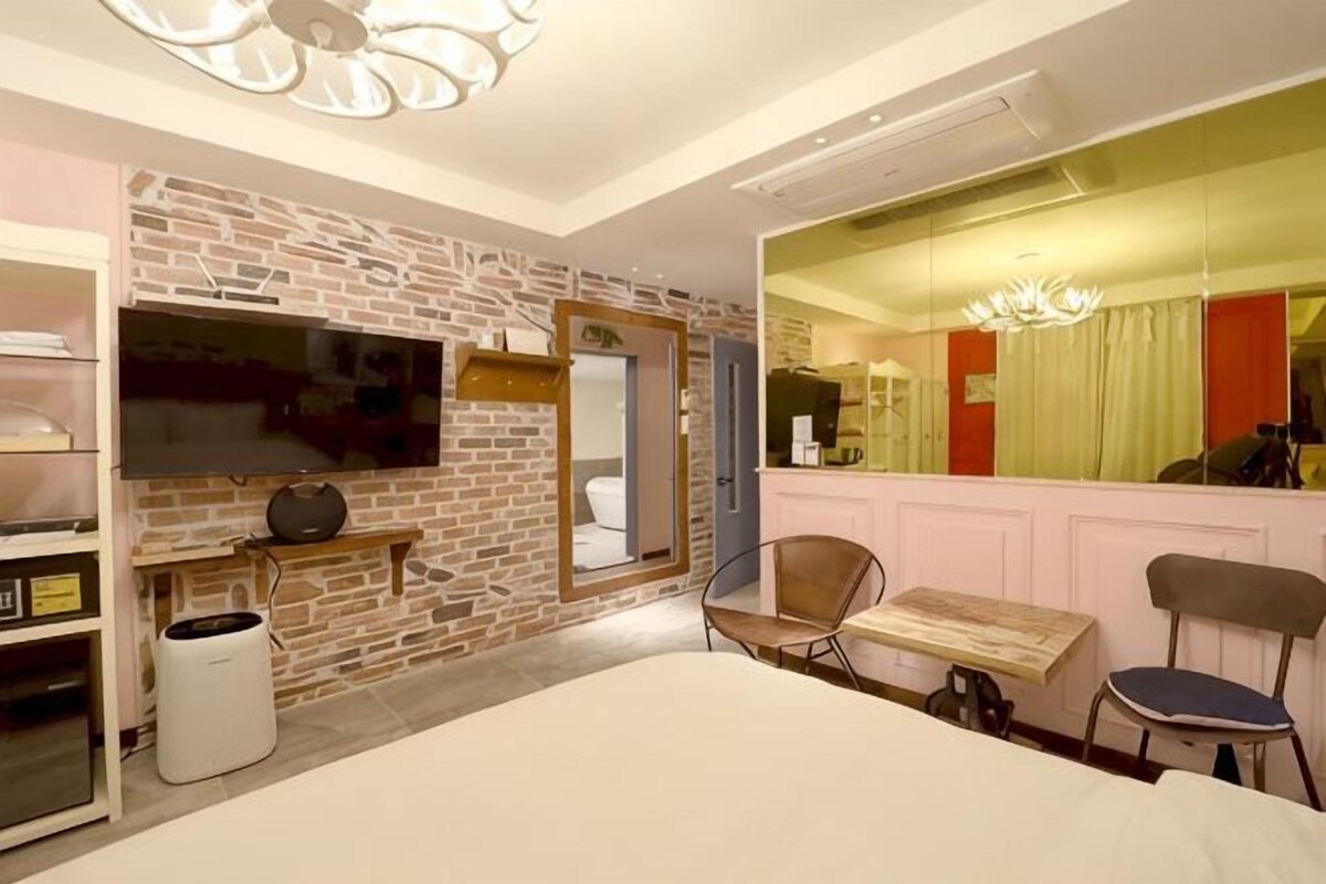 Habitación de hotel con pared de ladrillo, una cama, un televisor, un espejo, un escritorio y una silla.