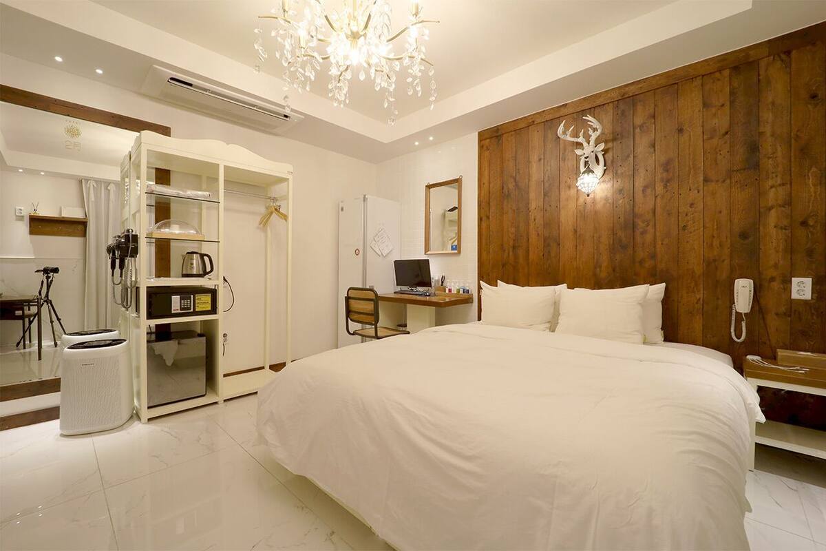 A modern bedroom with a large bed, a wooden accent wall, a desk with a computer, and a mirror.