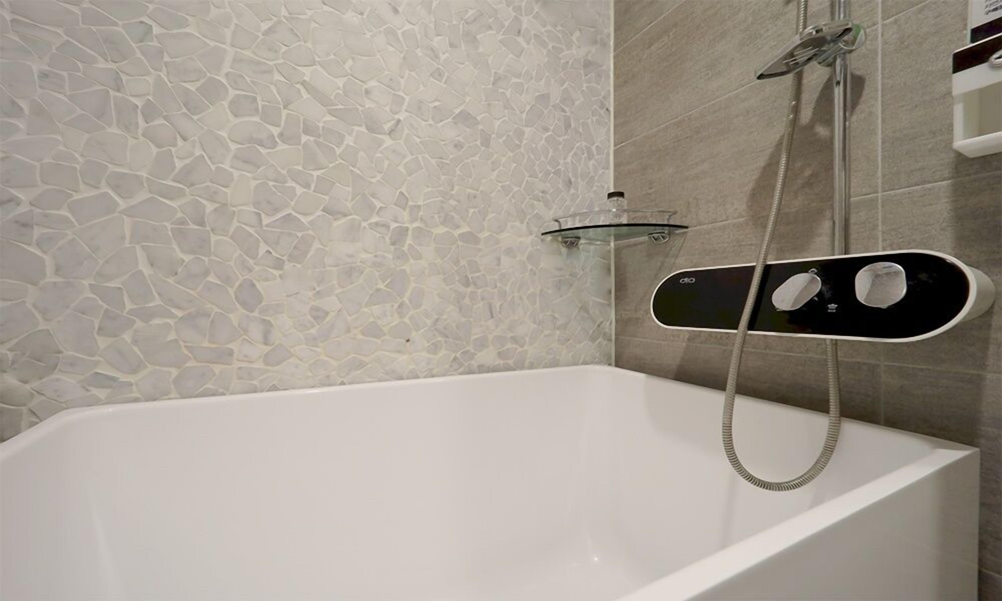 Un baño moderno con pared de diseño de piedra, una bañera blanca y un cabezal de ducha de mano.