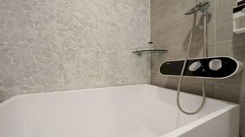 Un baño moderno con pared de diseño de piedra, una bañera blanca y un cabezal de ducha de mano.