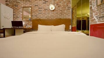 Habitación de hotel con pared de ladrillo, cabecero de madera, cama con ropa blanca, escritorio con computadora y espejo.