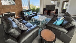 Een moderne woonkamer met leren banken, een flatscreentelevisie en een groot raam met uitzicht op de omgeving.