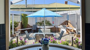 Een uitzicht op een terras met buitenmeubels, een blauwe parasol en een bloevas.