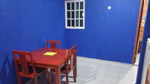 Een kamer met een blauwe wand, een wit raam, een rode tafel met vier stoelen en een vloer van witte tegels.