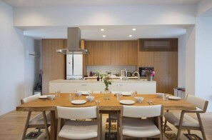 A modern kitchen with wooden cabinets, a central island, and a dining area with a wooden table and white chairs. - K Seaveiw 250㎡ ONNA 2 big suites, 3 full bath 3F (Nakadomari, Onna, Kunigami-gun)
