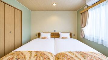 Uma cama de casal com colcha florida, cabeceira de madeira e janela com cortinas.