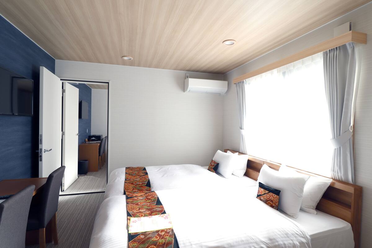Hotelkamer met een groot bed, een bureau met stoel, een kledingkast en een badkamer die door een geopende deur zichtbaar is.
