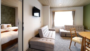 Una habitación de hotel moderna con un sofá, una mesa de comedor y un televisor montado en la pared.