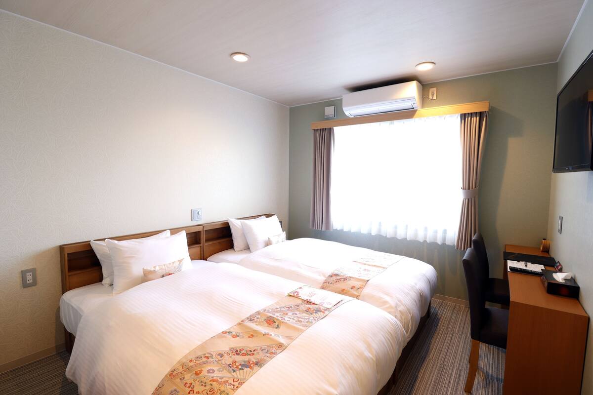 Een hotelkamer met twee bedden, een bureau en een airconditioner.