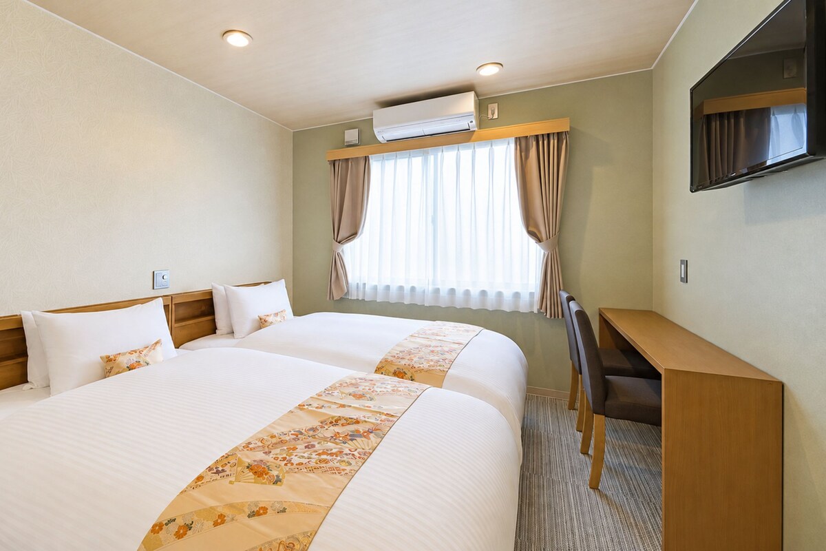 Una habitación de hotel con dos camas, un escritorio y un equipo de aire acondicionado.