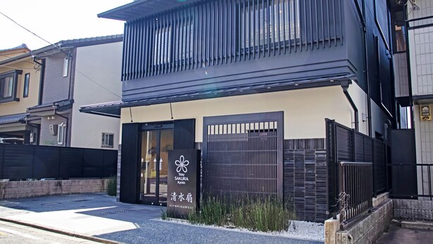 Un edificio moderno con fachada negra y beige, que presenta una entrada amplia con puerta de vidrio y un letrero que dice "Stay SAKURA Kyoto".