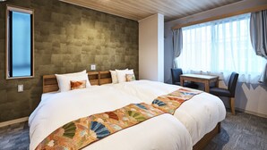 Una habitación de hotel con una cama grande, un cabecero de madera, una mesita con sillas y un ventanal con cortinas.