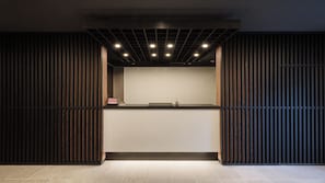 Una zona de recepció amb mostrador, línies verticals i llums al sostre.