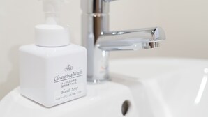 A bathroom sink with a white bottle of cleansing wash and a chrome faucet.