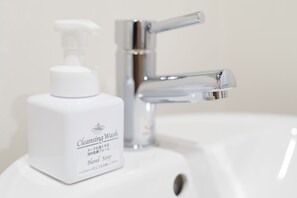 Un lavamanos de baño con una botella blanca de limpiador y un grifo cromado.