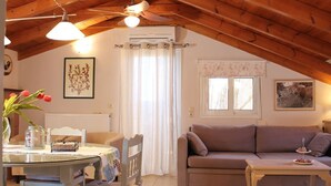 Ett mysigt vardagsrum med ett träpanelat tak, en soffa, ett bord och en matplats med stolar och en vas med blommor.