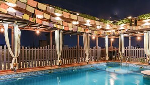 Una piscina interior con cerramiento de madera, una pérgola con banderas de colores y suelo de baldosas.
