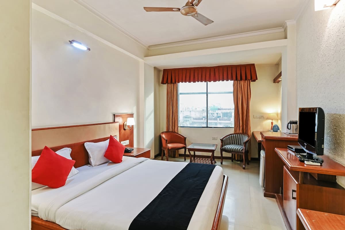 Una habitación de hotel con una cama, un escritorio, un televisor y una ventana con cortinas.