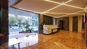 Un vestíbulo moderno con piso de mármol, una recepción y vista a la calle.