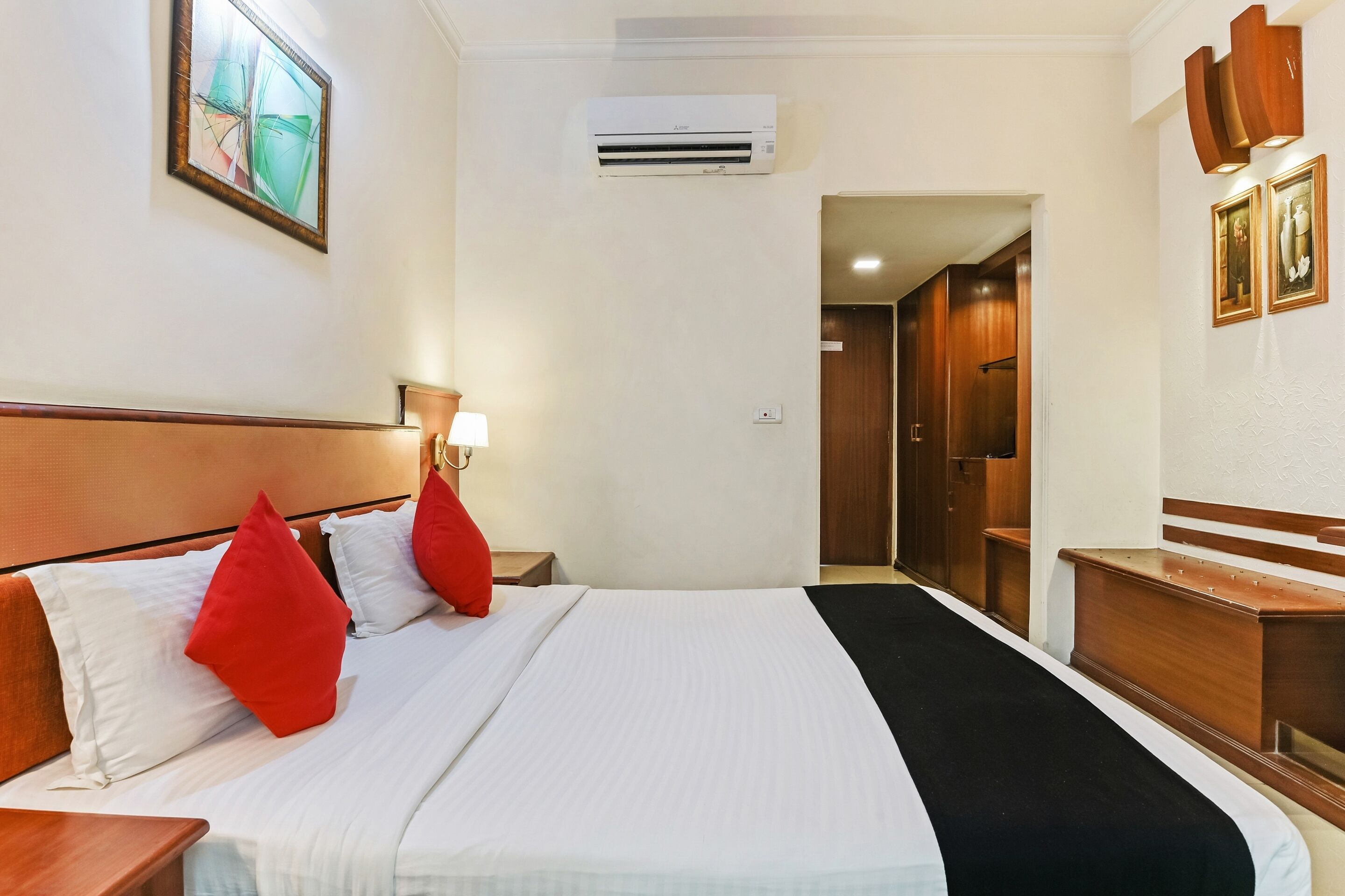 Une chambre d’hôtel comprenant un lit, une table de chevet, une lampe, un appareil de climatisation et une armoire en bois.