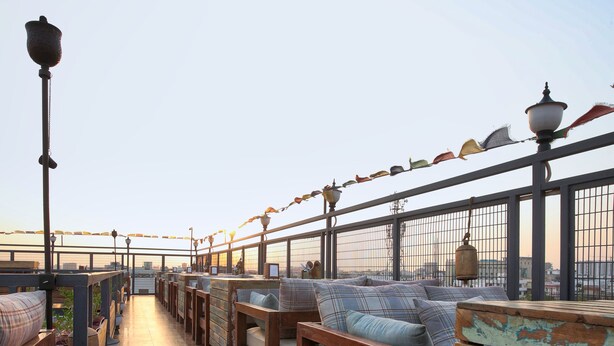 Una terraza con bancos y mesas de madera, barandilla y vista panorámica de la ciudad.