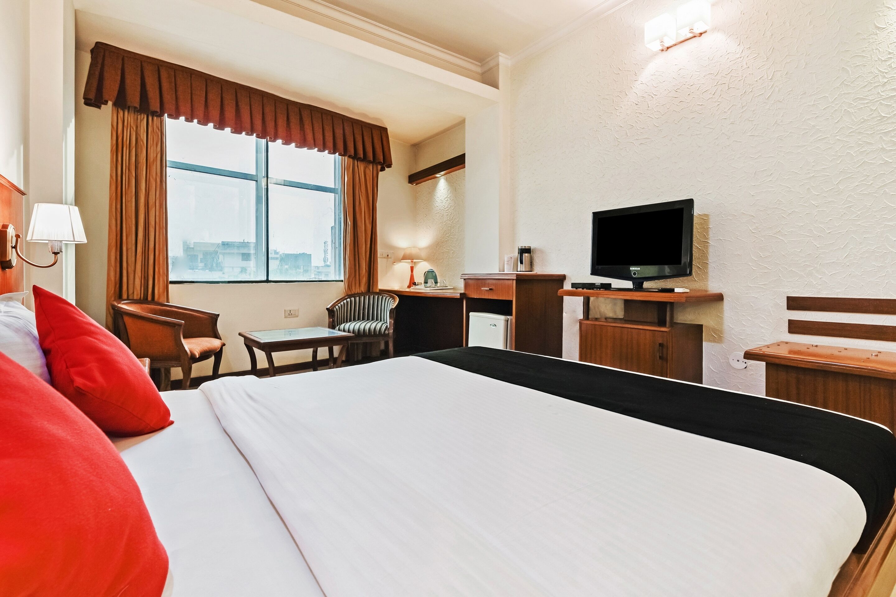Une chambre d’hôtel avec un grand lit, un bureau, une chaise, une télévision et une fenêtre avec des rideaux.