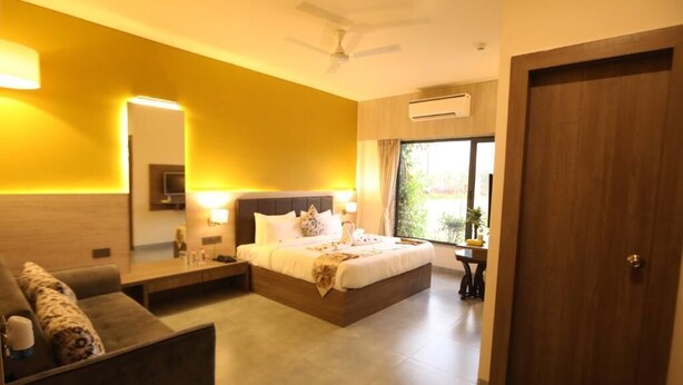 A hotel room with a bed, bedside table, lamp, and a view of the outdoors. - Solitaire Resort (Udaipur)