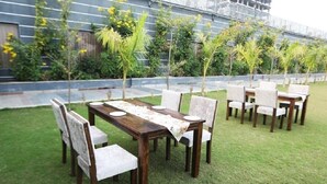 An outdoor dining area with a wooden table and chairs, surrounded by a well-maintained lawn and various plants. - Solitaire Resort (Udaipur)