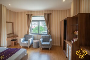 A hotel room with striped wallpaper, a bed, two armchairs, a small table, a wooden wardrobe, and a window with curtains. - Linh Phuong 3 Hotel (Can Tho)
