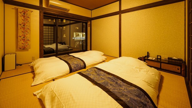 Une pièce de style japonais traditionnel, avec un sol recouvert de tatamis, une porte coulissante et un lit agrémenté d’une couvre-lit à motifs.