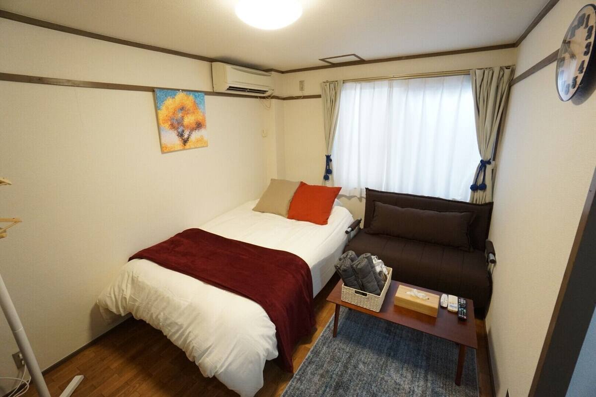 Une pièce de taille modeste comprenant un lit, un canapé, une petite table avec un panier, et une horloge au mur.