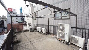 A rooftop with multiple air conditioning units, a metal railing, and a view of surrounding buildings. - Apartment BS Kawara Heights Namba (Osaka)