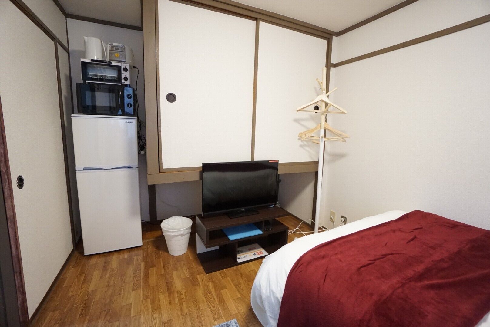 A compact room with a bed, a television on a stand, a microwave, and a small kitchenette area.