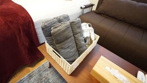 A neatly arranged room with a bed, a brown sofa, a small table with a basket of towels, and a bedside table with a tissue box and a remote control. - Apartment BS Kawara Heights Namba (Osaka)