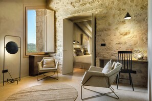 Una habitación con pared de piedra, un ventanal grande, una lámpara de pie redonda, un sofá y una silla.