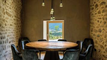 A round wooden table with six chairs, a stone wall, and a view through a doorway.